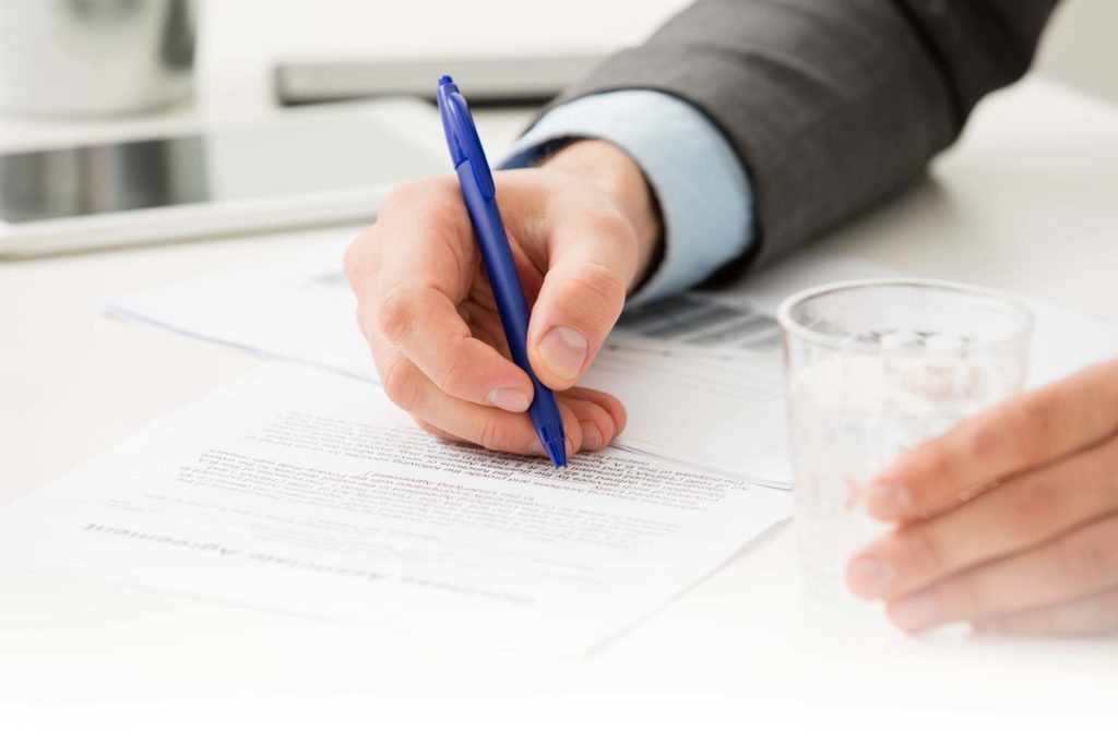 Close up of businessman signing contract with blue ballpoint pen