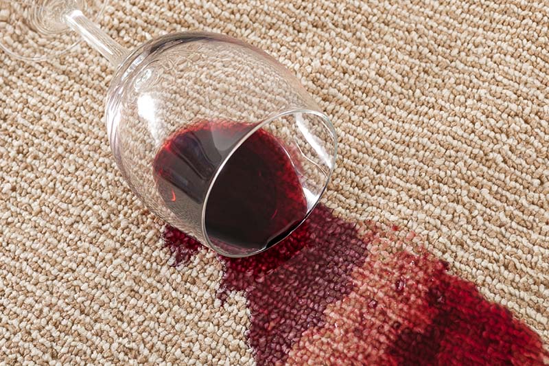 Home mishap and domestic accident concept with close up of  a spilled glass of red wine on brown carpet