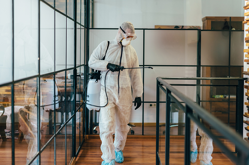 Man in protective suit and face mask spraying for disinfection in the office
