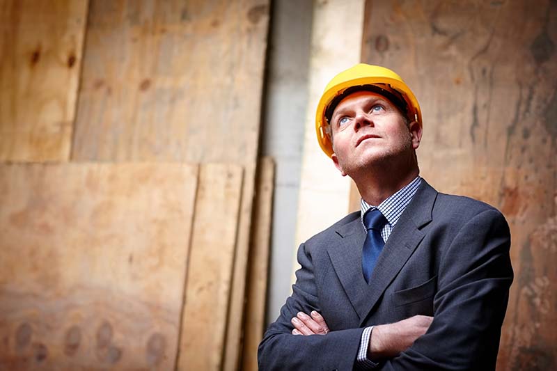 Portrait of mature male engineer looking upwards with his arms crossed at construction site