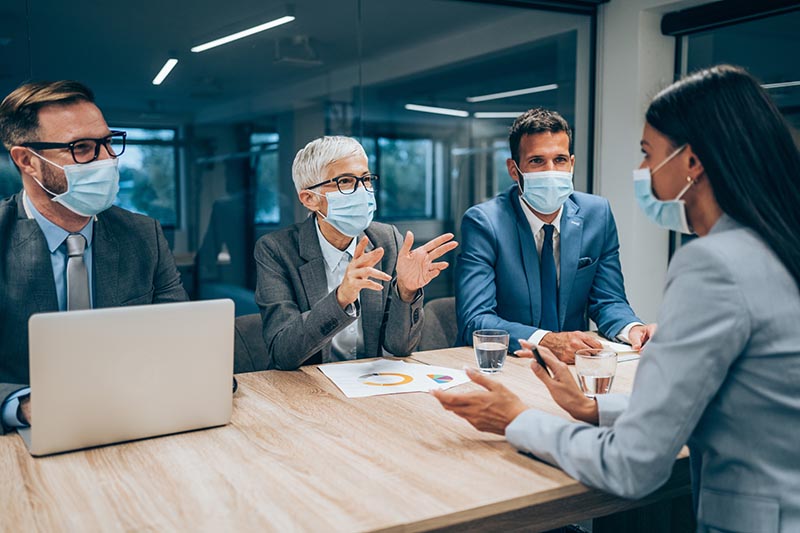 Shot of a group of businesspeople with protective face masks interviewing a candidate in an office. Young  businesswoman during job interview in modern office.