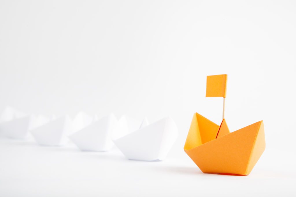 Leadership concept with orange paper ship leading among white
