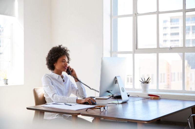 young-black-woman-talking-on-phone-at-her-desk-in-an-office-picture-id693722544