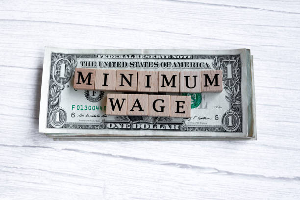 Minimum wage word written on wood block with American Dollar-bills. Directly above. Flat lay. Employment concept.