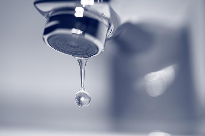 Dripping faucet close-up with drop of water. Blue toned image.