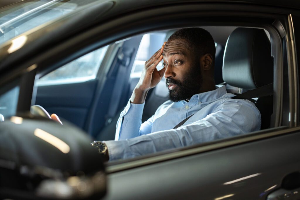 A man sits in his car at night with a stressed and concerned expression, holding his hand to his forehead. The scene conveys emotions of worry, tension, or frustration experienced in a personal moment.