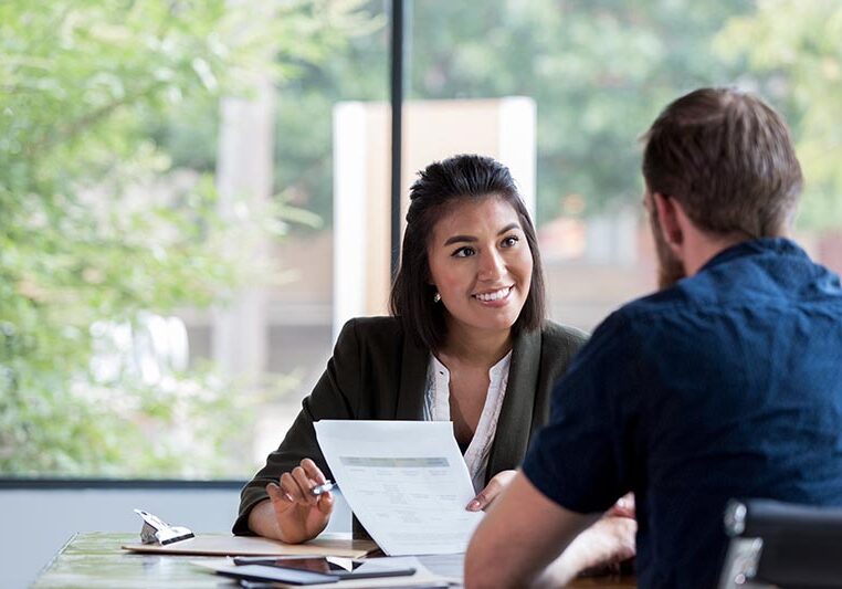Hispanic businesswoman smiles while showing a document to a male associate.