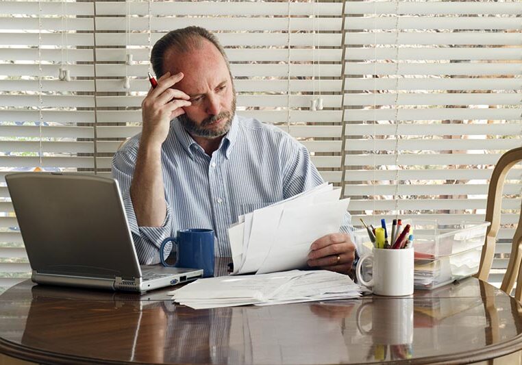 This middle age male sits at the kitchen table frustrated with stack of bills to pay and mounting debt.