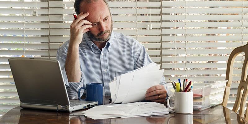 This middle age male sits at the kitchen table frustrated with stack of bills to pay and mounting debt.