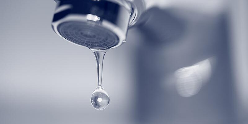 Dripping faucet close-up with drop of water. Blue toned image.