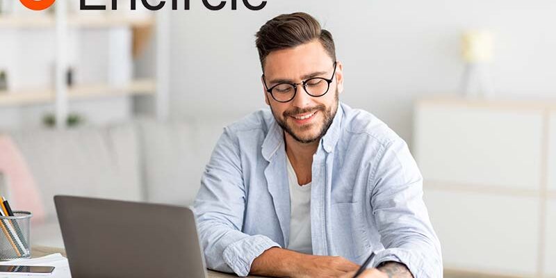 Happy millennial man looking for job online, sitting at table, using laptop and taking notes, living room interior, free space. Excited guy working online from home, remote job