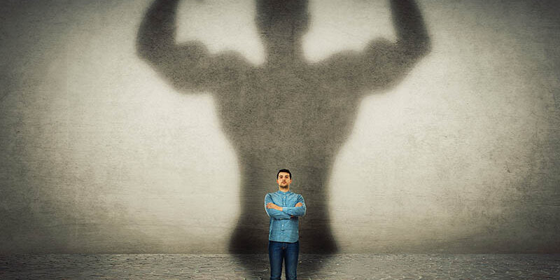 Confident businessman imagine himself a powerful hero, casting shadow of big strong muscular bodybuilder showing his biceps. Inner strength, leadership qualities. Business development.