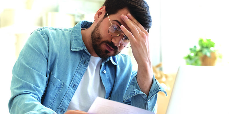 Upset frustrated young man reading bad news in postal mail letter paper document sit at home table, depressed stressed guy worried about high bill tax invoice, overdue debt notification money problem