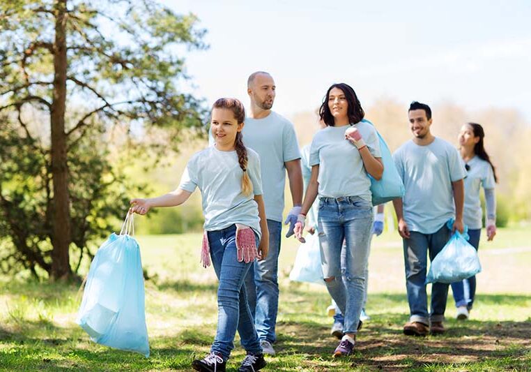 volunteering, charity, cleaning, people and ecology concept - group of happy volunteers with garbage bags walking in park