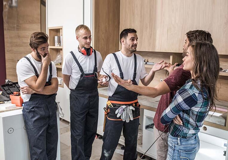 Young displeased couple talking to construction workers who passed their deadline for home renovation.