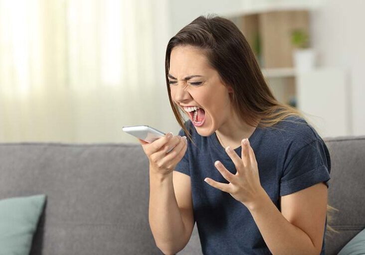 Furious woman shouting to smart phone sitting on a couch in the living room at home