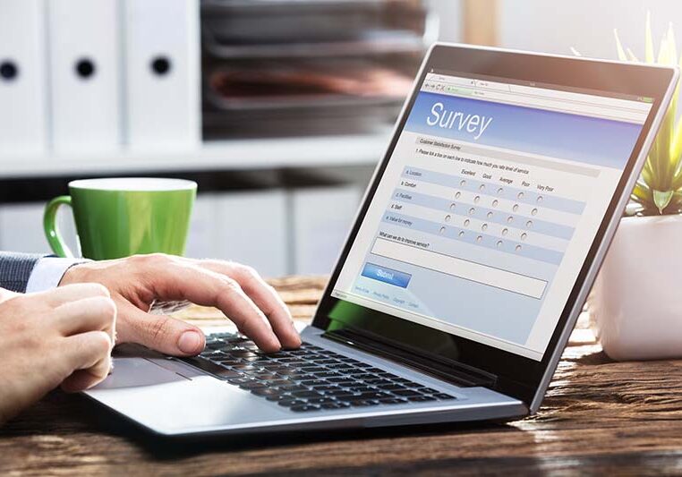 Close-up Of A Businessperson's Hand Filling Online Survey Form On Laptop Over Wooden Desk