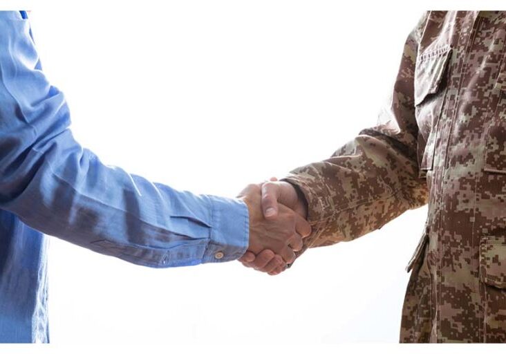 Military person and civilian shaking hands standing on white background