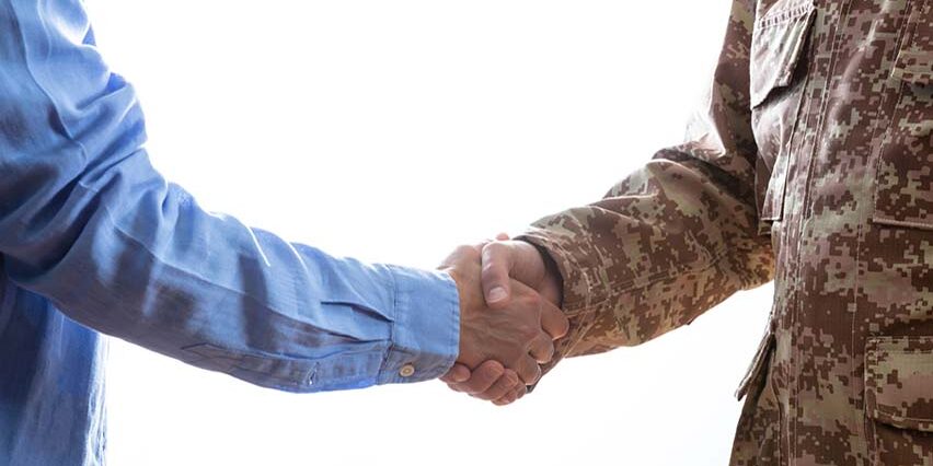 Military person and civilian shaking hands standing on white background