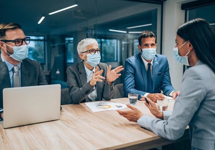 Shot of a group of businesspeople with protective face masks interviewing a candidate in an office. Young  businesswoman during job interview in modern office.