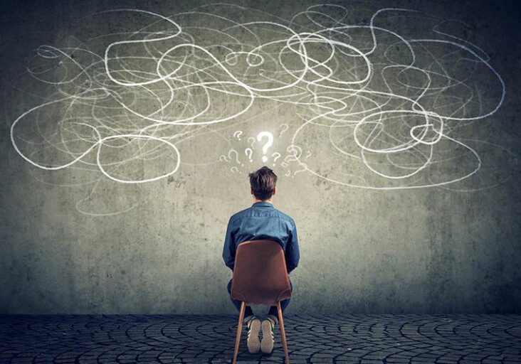 Back view of a thoughtful young businessman sitting on chair looking at a scribble on a wall feeling confused with too many questions