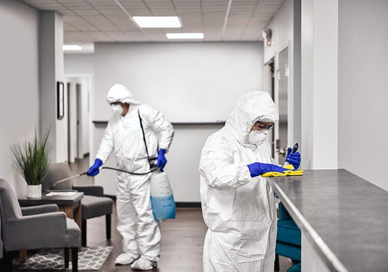 Two people in protective workwear cleaning and disinfecting offices.
