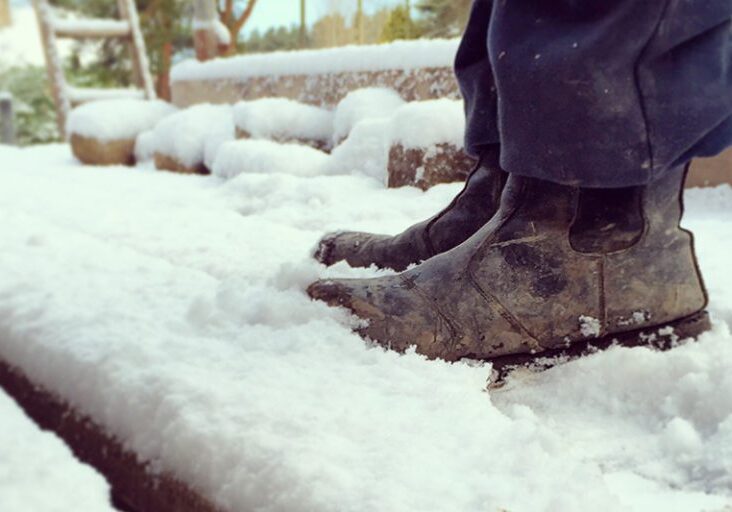 Builder standing on snow covered scaffold planks. Square image with main focus on the boots