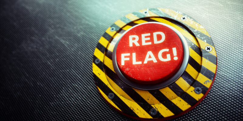 A 3D render of a conceptual mechanism with a red button and the words "RED FLAG" written on it, placed on an dark industry grid. The image can represent various concepts of danger, from political, military.. to dangers in realtionships - the so called "red flag" metaphor.