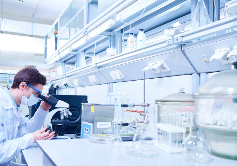 Young scientist examining sample with microscope in modern laboratory