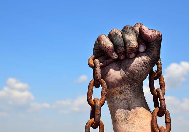 Rusty iron chain in human male right hand against the blue sky